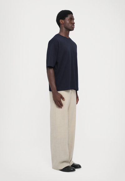 Μπλούζα κοντομάνικη ναυτικού τόνου από μαλακό υλικό, σε συνδυασμό με ελαφριά μπεζ παντελόνια wide-leg και μαύρα παπούτσια. Απλή, άνετη εφαρμογή.