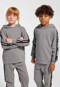 Grå hættetrøjer med lange ærmer, med sorte logo-accenter langs armene. Begge er kombineret med matchende grå bukser. Glat tekstur.