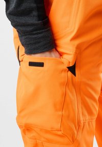 Oranje werkbroeken van duurzaam materiaal, met contrasterende zwarte accenten, een zijzak en dikke stiksels voor extra sterkte.
