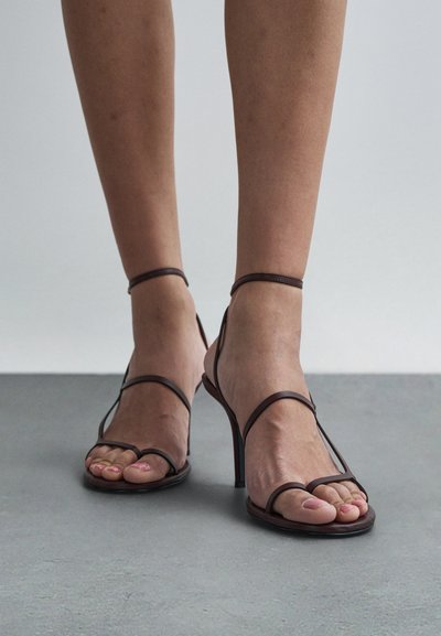 Hnědé sandály na vysokém podpatku s tenkými pásky. Design s otevřenou špičkou, elegantní silueta, hladká textura a minimalistický styl.