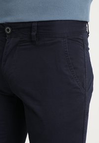 Pantaloni in cotone blu navy con taglio dritto, dotati di tasca frontale, passanti per cintura e chiusura frontale con bottone. Tessuto liscio.