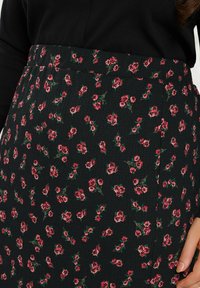 Musta hame, jossa on pieniä vaaleanpunaisia kukkakuvioita, teksturoitu kangas, istuva vyötärö ja sivusaumadetaljit. Suunnittelussa on hienovaraisia vihreitä vivahteita.