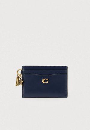 Navy leather cardholder with a gold logo, curved stitching, and decorative charms: a rectangular shape with a smooth texture.
