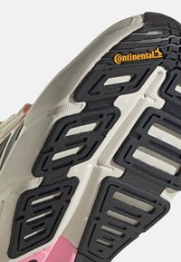 Semelle de chaussure en caoutchouc noir à motifs multiples, avec une intercalaire crème et un accent rose. Présente un marquage Continental. La texture montre un design de traction.