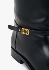 Czarny skórzany botek za kostkę o eleganckiej sylwetce, z ozdobną złotą klamrą na czarnym pasku oraz niskim klockowym obcasem.