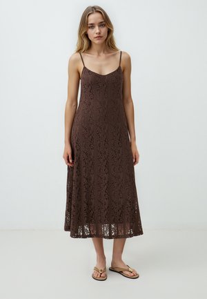 Robe maxi en dentelle brune à fines bretelles, dotée d'une texture à motif et d'une silhouette fluide. Portée avec des sandales plates.