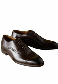 Zapatos de vestir de cuero marrón oscuro con un acabado suave, diseño con cordones, detalles de brogue y puntera redondeada. Acentos texturizados en los lados.