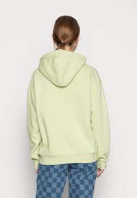 Ljusgrön oversize hoodie med dragsko på huvan och ribbade manschetter, i kombination med blå rutiga byxor. Mjuk textur, avslappnad passform.