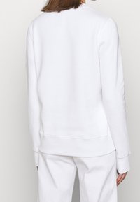 Bílá mikina s kulatým výstřihem, dlouhými rukávy a žebrovanými manžetami. Hladká textura, uvolněný střih a čistý, minimalistický design.