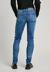 Úzké modré džíny z denimu se světlejším praním, s dvěma zadními kapsami a malou logem na pase. Hladká textura.