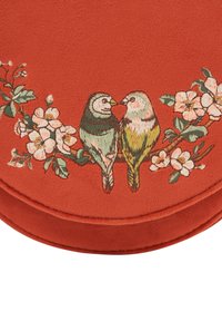 Rdeča faux surovinska torbica z vezenimi zelenimi in rumenimi pticami, obdanimi s cvetličnimi motivi. Krožna oblika z gladko teksturo.