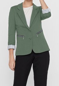 Zelený blazer se strukturovaným designem, zapínáním na jediný knoflík, zipovými kapsami a ohrnutými pruhovanými rukávy. Měkká látka s hladkým povrchem.