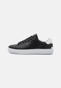 Czarne syntetyczne sneakersy z białym akcentem na pięcie, gumową podeszwą, okrągłym noskiem oraz sznurowanym designem z logo po boku i na języku.