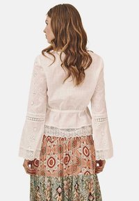 Blusa blanca de manga larga con bordados y encaje en las mangas y la cintura, combinada con una falda de colores múltiples y estampado.