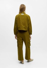 Giacca cropped verde oliva e pantaloni cargo a gamba larga. Tessuto resistente, design minimalista, con molteplici tasche e un'etichetta sul retro.