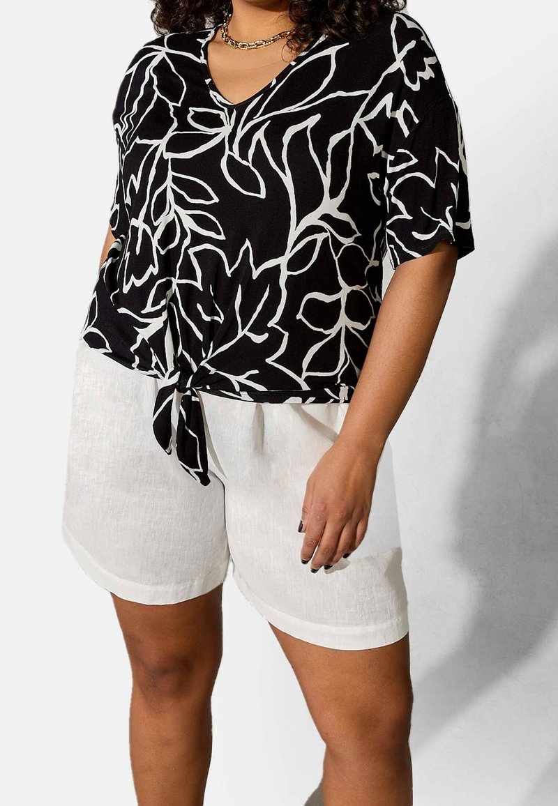 Black and white floral print top with a V-neck and tie at the waist, paired with light linen shorts in white. Smooth texture.