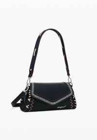 Borsa a mano in pelle nera con un'ala triangolare, cuciture decorative e tracolla rimovibile. Finiture in argento e accenti a contrasto.