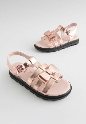 Rosenvergoldete Sandalen mit mehreren Riemen, einer dekorativen Schleife und einer schwarzen Gummisohle. Verfügt über einen verstellbaren Schnallenriemen für einen sicheren Sitz.