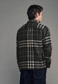 Chaqueta de lana a cuadros en gris oscuro con detalles en crema y beige. Presenta un cuello clásico y un corte relajado con bolsillos laterales y cierre de botones.