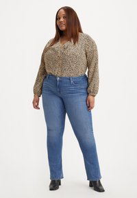 Blusa a fantasia leopardata con scollo a V, maniche lunghe e vestibilità rilassata, abbinata a jeans skinny blu e stivaletti neri alla caviglia.