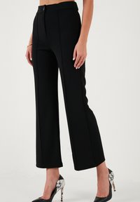 Black wide-leg trousers with a smooth texture, featuring front seams and a fitted waistband. Paired with black and white high-heeled shoes.