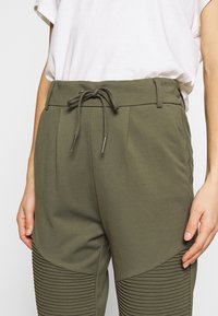 Olivgrüne Jogginghosen mit Kordelzugbund, Seitentaschen und geripptem Muster am Unterschenkel. Hergestellt aus weichem, dehnbarem Material.