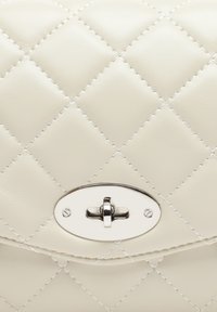 Borsa a tracolla in pelle crema trapuntata con una chiusura ovale argentata e cuciture bianche a contrasto, caratterizzata da una texture liscia e un motivo geometrico a rombi.
