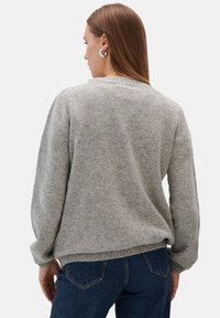 Szary sweter z dzianiny o luźnym kroju, z prążkowanymi mankietami i dekoltem. Połączony z ciemnoniebieskimi dżinsami, które prezentują teksturowany materiał.