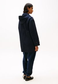 Parka impermeabile blu navy con cappuccio, polsini delle maniche con bottone e taglio dritto, abbinata a pantaloni jogger blu scuro e scarpe nere.