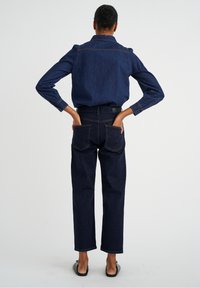 Donker denim shirt en broekenset, met een gestructureerd ontwerp, lange mouwen en een ontspannen pasvorm. De stof heeft een gladde textuur en duidelijke stiksels.