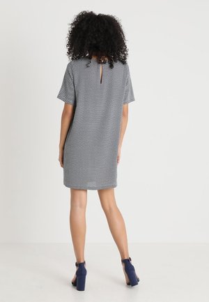 Vestido de manga corta con un patrón geométrico en azul marino y blanco, que presenta un detalle de escote en la espalda. Tejido suave, corte relajado, longitud por encima de la rodilla.