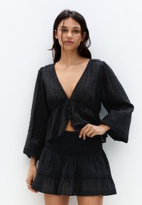 Top corto nero con maniche a campana lunghe, scollatura a V e bottoni. Abbinato a una gonna a balze a strati coordinata con vita arricciata.