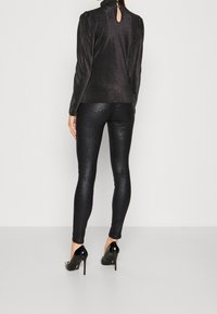 Svart glittrig topp med hög hals och puffärmar samt nyckelhålsdetalj, kombinerad med åtsittande svarta glittriga leggings och svarta högklackade skor.