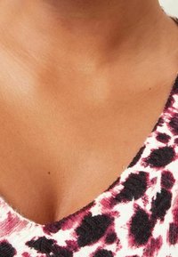 Pull en V avec un motif léopard en blanc, noir et bordeaux. Texture douce et tissu légèrement extensible. Gros plan du col.