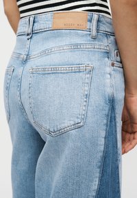 Ανοιχτό μπλε τζιν ψηλόμεσο με πίσω τσέπες και δερμάτινη ετικέτα "Noisy May", φορεμένο με ασπρόμαυρο ριγέ τοπ.