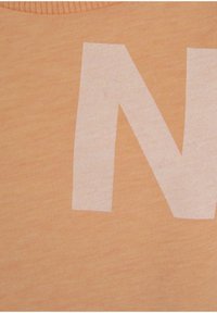 Perzikkleurig T-shirt gemaakt van een zachte, gestructureerde stof met een grote witte letter "N" in een vet, bloklettertype.