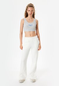 Grijze cropped tanktop met de opdruk "NEW YORK 1994", gecombineerd met witte, hoge, flared sweatpants. Glad materiaal, casual pasvorm.
