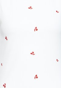 Tissu blanc orné de petits motifs floraux rouges brodés, répartis uniformément sur toute la surface.