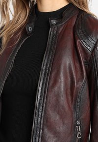 Bordeauxfarbene Leder-Motorradjacke mit diagonalen, gesteppten Schulterakzenten, Metalldruckknopfverschluss und Druckknopfdetails.