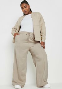 Beige, yläosastaan väljähkö bomber-takki, jossa vetoketju ja sivutaskut, yhdistettynä vastaaviin leveälahkeisiin collegehousuihin. Sileä kangas, rento malli.