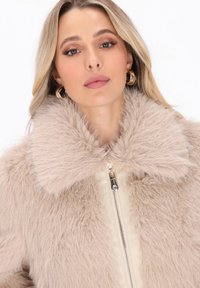 Lys beige faux fur jakke med bred krave, frontlynlås og glat inderfor; blød tekstur og luksuriøst udseende.