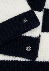 Wełniany sweter z poziomymi paskami w kolorze granatowym i kremowym, o prążkowanej fakturze i metalowymi guzikami z okrągłym wzorem.