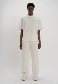 Jasnobeżowy, oversize t-shirt z okrągłym dekoltem i krótkimi rękawami, w komplecie z dopasowanymi, luźnymi spodniami dresowymi. Oba elementy posiadają minimalne oznaczenia marki.