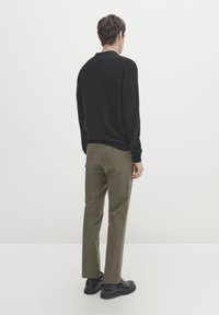 Maglione nero a trama con orlo a coste, abbinato a pantaloni verde oliva e scarpe nere. Vista da dietro su uno sfondo semplice.
