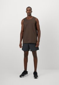 Camiseta castanha sem mangas e calções texturizados cinza escuro, usados com sapatilhas de corrida pretas. Design simples, adequado para desporto ou vestuário casual.