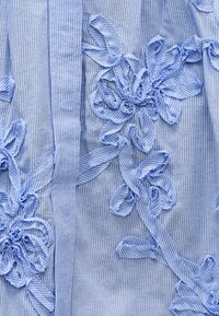 Ύφασμα με μπλε και άσπρες ρίγες με τρισδιάστατες ανθικές απλικέ κατασκευασμένες από μαζεμένο και στριμμένο υλικό.