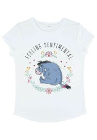 Bílý tričko s krátkým rukávem, na kterém je modrá ilustrace Eeyorea s textem "CÍTÍM SE SENTIMENTÁLNĚ" a květinovými akcenty v růžové a zelené barvě.