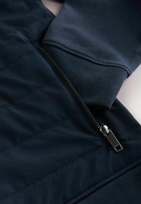 Granatowa polarowa kurtka z teksturowanym, wyściełanym przodem, ściągaczami na mankietach oraz eleganckim zamkiem z metalową zakładką.