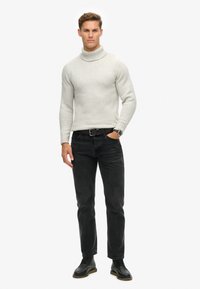 Lys grå strikket turtleneck trøje med ribbede manchetter, parret med sorte slim-fit jeans og sorte snørebåndssko, båret med et bælte.