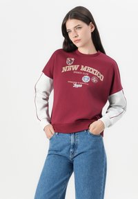 Bordeaux sweatshirt met witte mouwen, voorzien van een grafische print en geborduurde tekst "NEW MEXICO SPORTS CLUB." Relaxte pasvorm, geribbelde zoom.